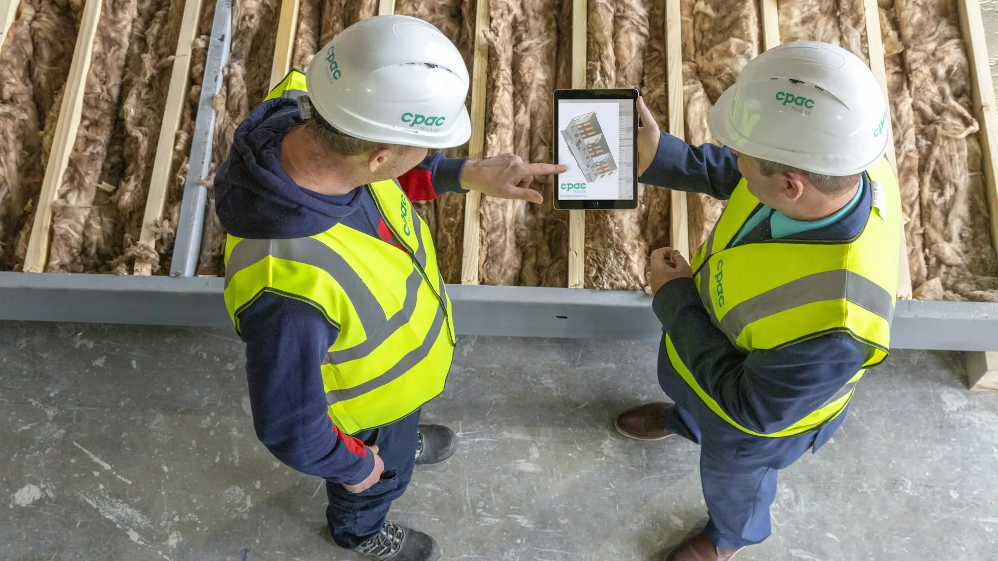 Contractors reviewing a plan on a tablet at a framed house (placeholder photo)